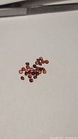 Loose diamond-cut almandine garnet gemstones scattered on a white surface with a pair of tweezers visible for size reference.