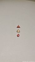 Three untreated natural tourmaline gemstones arranged vertically on a plain background: pinkish-orange trillion cut, pale yellow trillion to oval cut, and reddish-pink oval cut.
