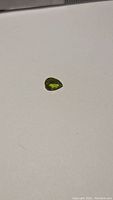 Pear cut natural apple green peridot gemstone on white background, showing general shape and color.