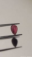 Photo of natural untreated deep pink pear-cut tourmaline held by tweezers showing the color and inclusions.