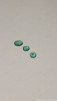 Three natural emerald gemstones in oval, cushion, and round cuts shown on plain background for clarity and detail.