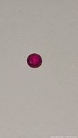 Round cut natural ruby gemstone on white background showing hot pink red color and clarity.