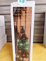 Retail box showing 14 inch green glitter Christmas tree with LED lights on and decorated with small ornaments and tinsel.