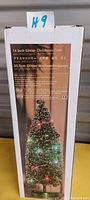 Box of 14 inch glitter Christmas tree with image showing tree decorated with colorful LED lights and some holiday decorations. Box includes product information in multiple languages.