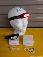 Photo of two black LED headlamps with adjustable straps, front lights featuring white and red LEDs, two USB charging cables, and original packaging boxes.