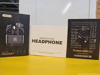 Photo showing three different wireless sport earbuds packages: TWS07-B, generic Wireless Sport Headphone, and Power Q20 Pro with noise level information on the box.