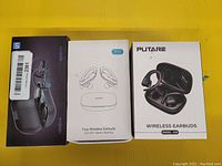 Three boxes of wireless sport earbuds arranged side by side on a yellow surface. Boxes show images and branding of the earbuds inside.