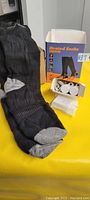Photo of black and grey heated socks along with rechargeable batteries and charger placed on yellow surface, next to product box.