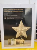 Photo of product box showing gold glitter star tree topper with battery powered LED lights and spring base.