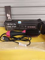 Photo of Vaslon One Step hair dryer and styler brush, out of box showing pink and black tool with brush bristles and power cord, with original box in background.