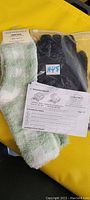 Two pairs of green Aeropostale fuzzy socks and one pair of black wired heated gloves with instruction manual laid out on a yellow surface.