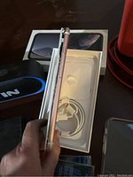 iPhone XR held sideways showing rose gold color with charger and box behind