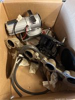 Box containing carburetor, intake manifold, air filter cap, and metal mounting flange.