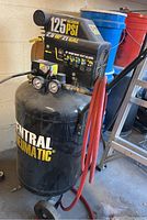 Full view of black Central Pneumatic vertical air compressor with coiled red hose.