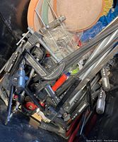Box containing various bar clamps and C clamps, showing several black-handle clamps and metal clamps in a pile