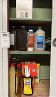 Photo showing cabinet shelves with large and small bottles including 99% isopropyl alcohol, Lysol, spray bottles and other cleaning supplies.