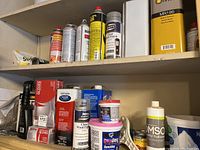 Shelf with cans and containers of wood finishes, stains, gloves, and other home repair materials.