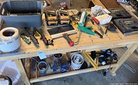 View of wooden workbench holding assorted hand tools including screwdrivers, caulking gun, small spotlight, small metal tools, and two Pittsburgh 40-piece tap and die sets in black plastic cases.