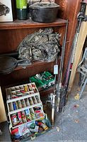 Overall view of fishing poles leaning against shelf, with tackle boxes and various fishing items on floor and shelf.