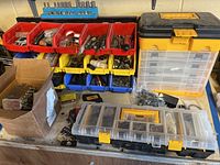 Overview of multiple plastic storage bins and toolboxes filled with various hardware items on a shelf.