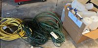 Yellow and green extension cords with spray bottles in a box on garage floor