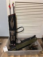 Overall shot of quiver leaning against closet door with plastic bin of assorted knife sheaths