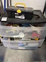 Plastic drawers filled with various hand tools and accessories, with a black toolbox on top.