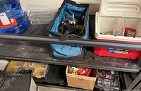 Steel shelf unit with various items including tool bags, cooler, water jug, and boxes containing ratchet straps and tools.