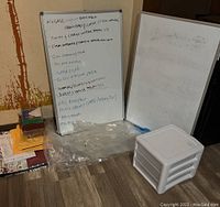 Two white boards, one with notes and one blank with marks, along with plastic drawer organizer and papers nearby.
