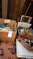 Wide view showing multiple boxes containing various household items including hand tools, door locksets and adhesive tapes.
