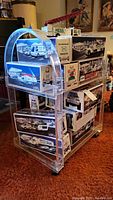 Full view of the clear acrylic rolling cart with multiple model vehicle boxes stacked on shelves to illustrate size and structure.