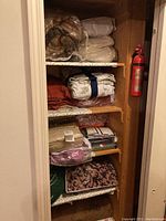 Several shelves filled with folded bed sheets and linens, some in clear plastic packaging, others folded and stacked in various colors and patterns.