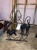 Black metal wire sitting cat wall decor with whiskers, metal base, accompanied by two black cast metal cat figures and dog bust in background.