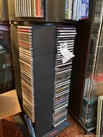 Side view of stacked CD cases showing multiple CDs in a black tower rack (rack not included)