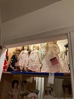 Wide shot of the porcelain baby dolls arranged on a shelf, showcasing approximately 11 dolls in vintage-style dresses and some with hats or bonnets.
