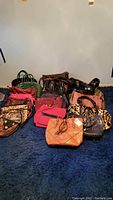 Full view of multiple handbags arranged on blue carpet showing various styles and colors including faux fur, faux leather, and patterned fabric.