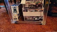 Bottom shelf of a clear cart showing stacked boxed Hess trucks and vehicles, emphasizing original packaging and packaging condition.