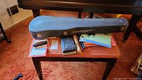 Overview of closed violin case on bench with flute case, recorders, harmonica and music books
