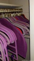 Closet rod filled with multiple felt hangers in purple, lavender, and pink colors with gold hooks