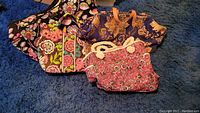 Multiple quilted fabric overnight bags and totes arranged on blue carpet showing different floral and paisley patterns.