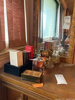 Photo showing assortment of perfume bottles and boxed perfumes on wooden surface next to mirror.
