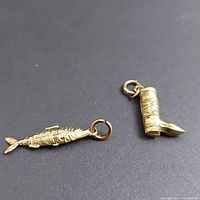 Close-up photo displaying the two charms, a fish and a boot, on a black background showing gold color and design details.
