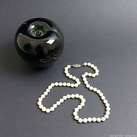 Pearl necklace displayed with a black spherical object for size reference, showing the entire 16 inch strand and decorative clasp.