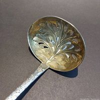 Close-up photo of the pierced gilt bowl with hand chased leaf design of the antique sterling silver tea strainer.