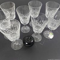 Set of eight crystal Waterford Lismore water goblets arranged on black surface, showing clear Lismore diamond and wedge cut pattern.