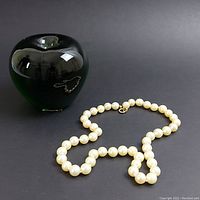 Overall view of the pearl necklace laid out with green glass apple for scale