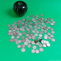 Overview of a large lot of silver British coins spread on a green background with a black spherical object for size reference