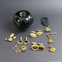 Overall view of lot with four pairs cuff links and three watch fobs arranged near green glass apple for size reference