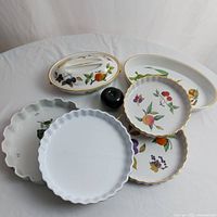 Full view of all six pieces showing fruit motifs and scalloped edges, with a green apple for scale.