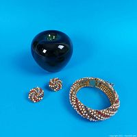 Overview of cuff bracelet and matching earrings against blue background with green apple for scale